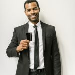 Smiling man in a black suit holding a credit card, symbolizing corporate finance.