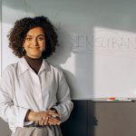 Smiling woman with curly hair standing by a whiteboard with 'insurance' written on it, conveying professionalism.